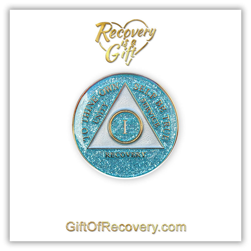 1 year AA medallion Aquamarine glitter, triangle is pearl white, to thine own self be true, unity, service, recovery, and roman numeral are embossed with 14k gold-plated brass, the recovery medallion is sealed with resin for a glossy finish that will last and is scratch free, pictured on a white 3x3 card with recovery is a gift going through an open heart at the top and giftofrecovery.com on the bottom, both in the color gold.