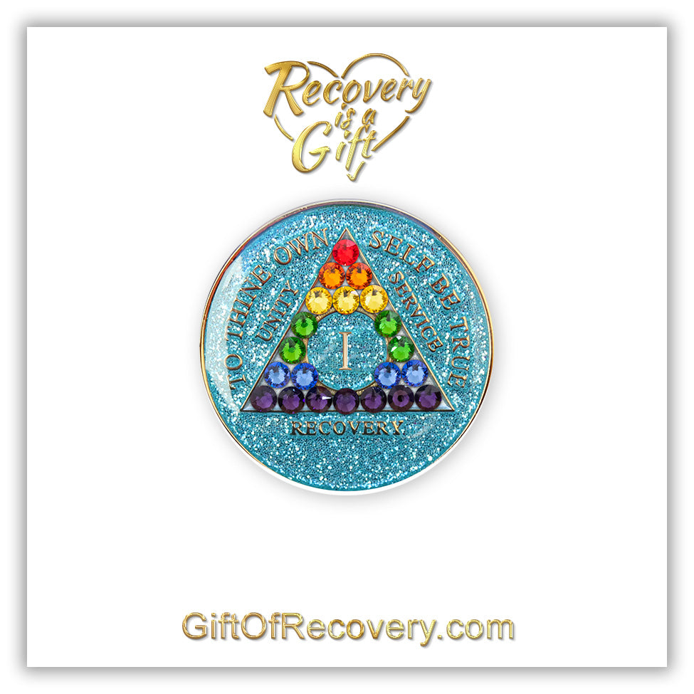 1 year deep sea aqua glitter AA medallion adorned with 21 genuine crystals representing the rainbow in the shape of the triangle to support renewal and growth on the journey of recovery, the AA moto is embossed with 14k gold-plated brass and sealed with resin for a glossy finish, featured on a white 3x3 card with recovery is a gift and giftofrecovery.com in the color gold.