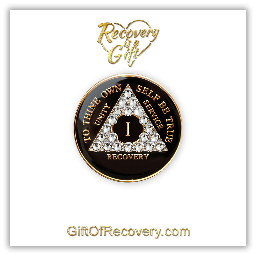 1 year AA medallion black onyx with 21 clear genuine crystals in the shape of the triangle, to thine own self be true, unity, service, recovery, and the roman numeral are embossed with 14k gold-plated brass, the recovery medallion is sealed with resin for a glossy finish that will last and is scratch proof, the medallion is featured on a white 3x3 card with recovery is a gift going through a heart at the top center and giftofrecovery.com at the bottom center, both written in the color gold.