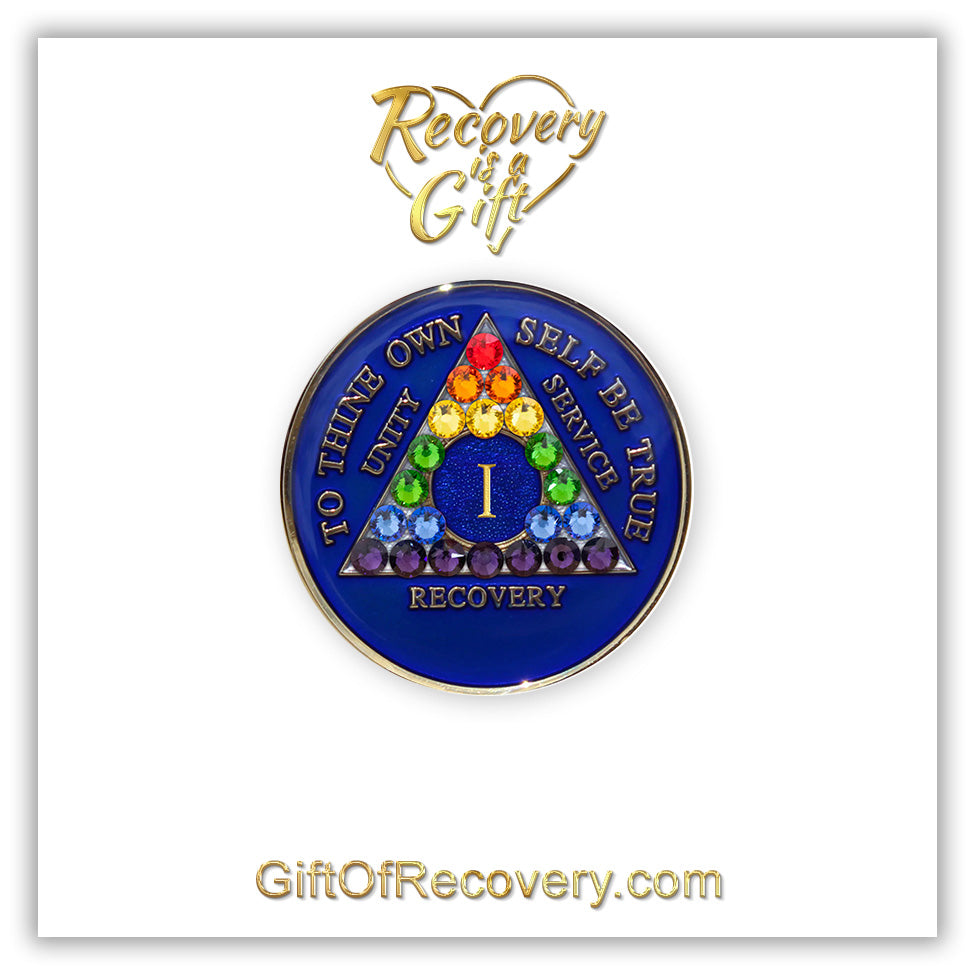1 year AA medallion Big Book blue with 21 genuine crystals in rainbow form and the shape of the triangle, representing renewal and growth in the program, AA slogan and three legacies embossed with 14k gold-plated brass, sealed with resin for a glossy finish, featured on a white 3x3 card with recovery is a gift going through an open heart and giftofrecovery.com on the bottom, both in the color gold.