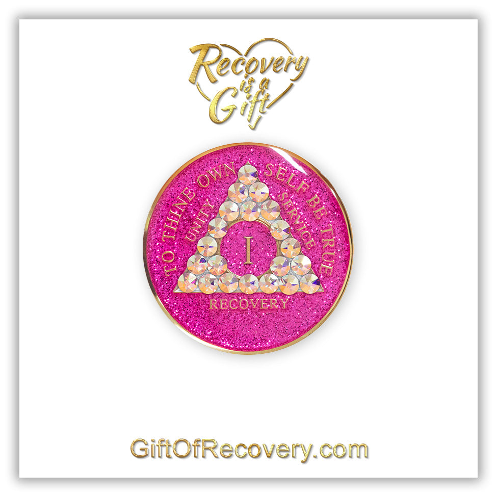 1 year AA medallion pink glitter princess adorned with 21 Aurora Borealis genuine crystals to bring out the sober princess in you the crystals are in the shape of the triangle, to thine own self be true and AA moto embossed with 14k gold-plated brass, recovery medallion is sealed with resin for a glossy finish that will last and is scratch proof, featured on a white 3x3 card with recovery is a gift and giftofrecovery.com in the color gold.