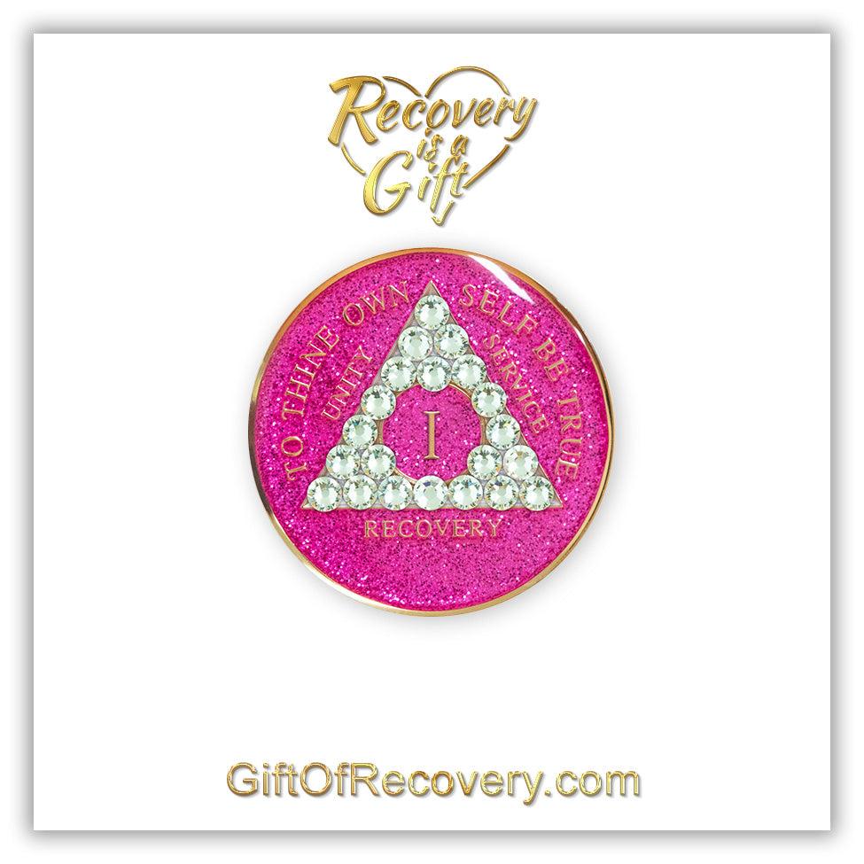 1 year AA recovery medallion in glitter princess pink and adorned with 21 diamond CZ genuine crystals shaped in the triangle to add sparkle to your sober princess journey in recovery, to thine own self be true, unity, service, recovery are embossed with 14k gold-plated brass and sealed with resin for a glossy finish that will last and is scratch proof, featured on a white 3x3 card with recovery is a gift, giftofrecovery.com in the color gold.