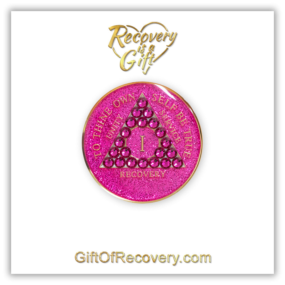1 year Princess Pink Glitter AA medallion with 21 genuine fuchsia crystals in the shape of a triangle in the center of the recovery medallion, and to thine own self be true, unity, service, recovery, the roman numeral in the middle, and the outer rim, embossed in 14k plated brass, the aa medallion is sealed in resin for a shiny finish, the recovery medallion is on a 3x3 white card with recovery is a gift going through a heart at the top and giftofrecovery.com at the bottom, all in color gold.