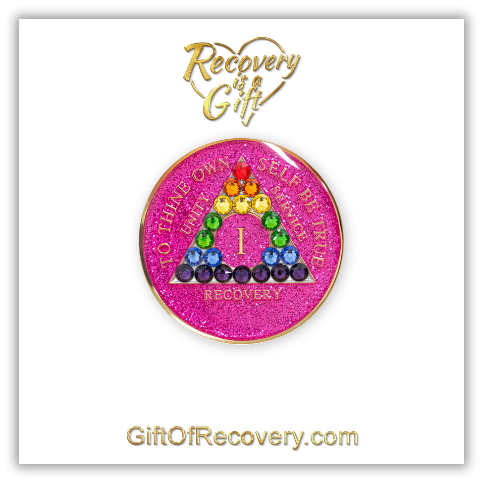 1 year AA medallion pink glitter princess with 21 genuine crystals in the colors of the rainbow to represent renewal and self-discovery, in the shape of the triangle, the AA moto is embossed with 14k gold-plated brass and sealed with resin, featured on a white 3x3 card with recovery is a gift going through a heat at the top and giftofrecovery.com at the bottom, both in the color gold.
