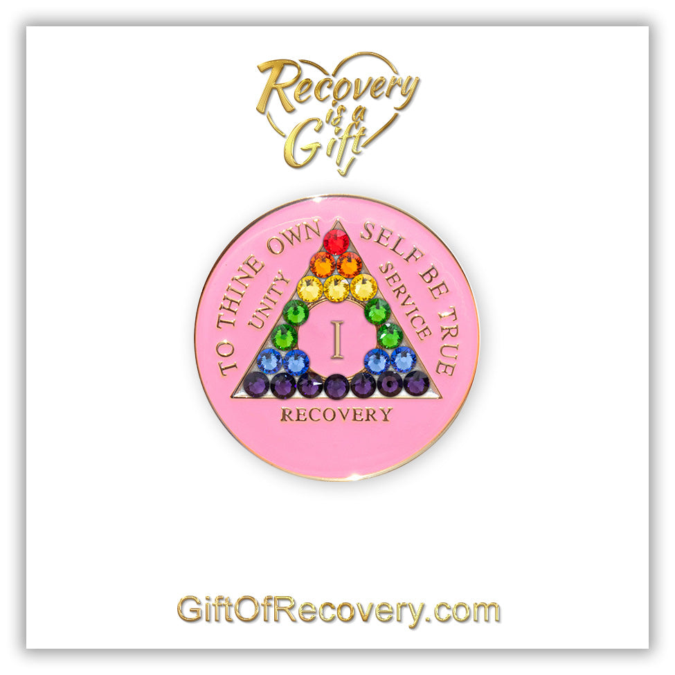 1 year AA medallion princess pink with 21 genuine crystals that form a rainbow in the shape of the triangle, to represent change through working the program, the AA slogan and three legacies are embossed with 14k gold-plated brass, sealed with resin for a shiny finish that will last, featured on a white 3x3 card with recovery is a gift going through an open heart at the top, and giftofrecovery.com at the bottom in the color gold.