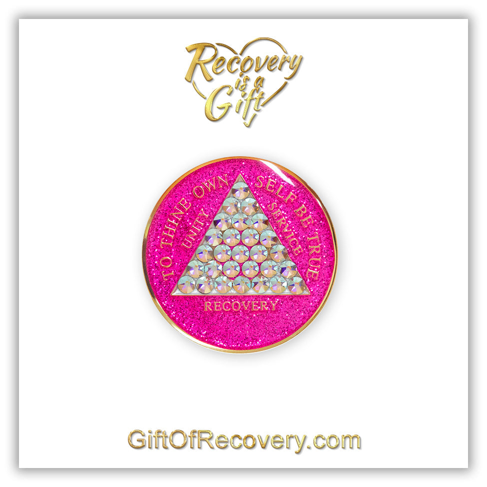 AA medallion princess pink glitter with 28 diamond CZ genuine crystals that form the triangle entirely, this is the timeless medallion, shine on with this beauty, we all have one day at a time, the AA slogan and three legacies are embossed with 14k gold-plated brass and sealed with resin for a glossy finish that will last and is scratch proof, pictured on a white 3x3 card with recovery is a gift going through an open heart at the top and giftofrecovery.com at the bottom, both in the color gold.