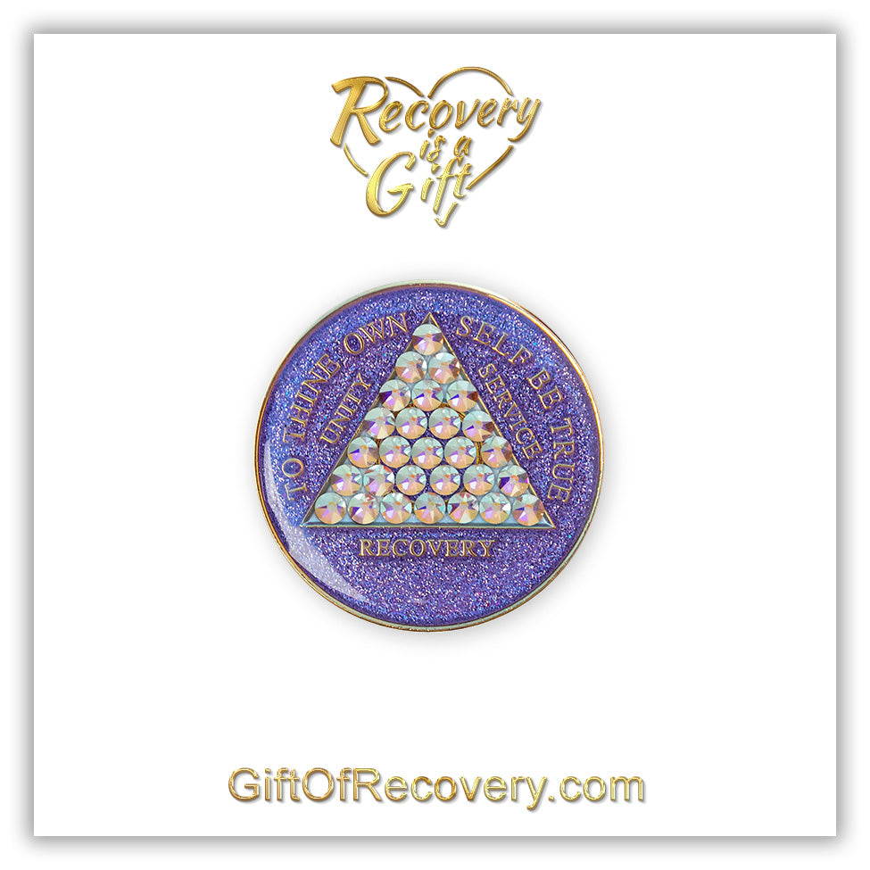 AA medallion amethyst purple glitter with 28 diamond CZ genuine crystals that form the triangle entirely, this is the timeless medallion, shine on with this beauty, we all have one day at a time, the AA slogan and three legacies are embossed with 14k gold-plated brass and sealed with resin for a glossy finish that will last and is scratch proof, pictured on a white 3x3 card with recovery is a gift going through an open heart at the top and giftofrecovery.com at the bottom, both in the color gold.