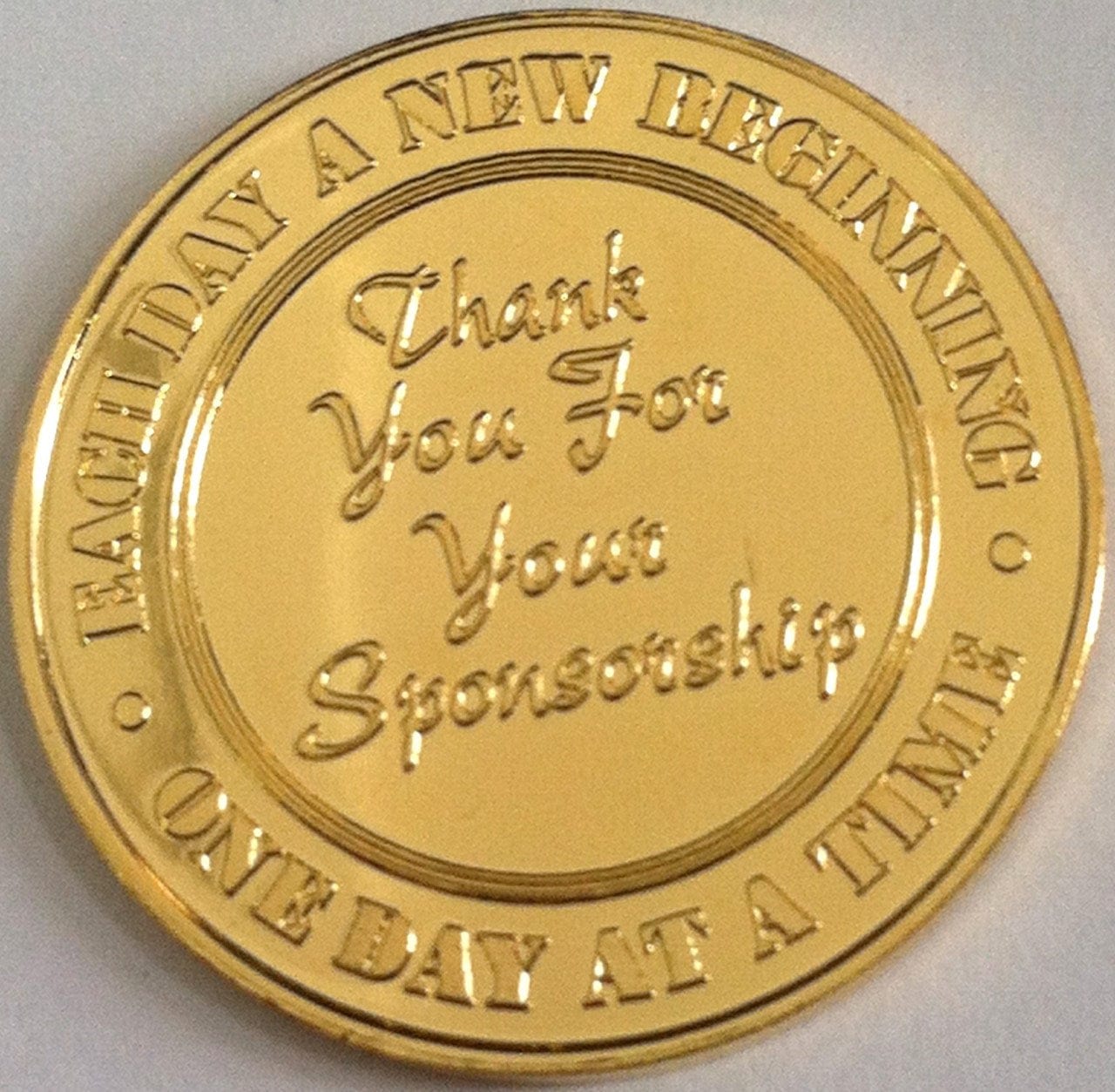 Back of gold-plated sponsorship recovery medallion with thank you for your sponsorship in the middle and each day a new beginning, one day at time around the edge.