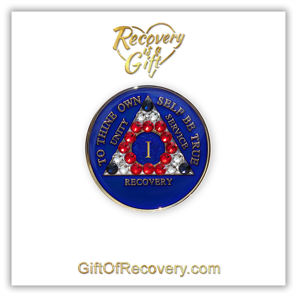 1 year AA medallion Big Book blue adorned with 3 sapphire, 6 diamond CZ, 12 red genuine crystals, red, white, blue, symbolizing proud to be an American, AA slogan three legacies are embossed with 14k gold-plated brass and sealed with resin for a glossy finish, seen on a white 3x3 card with recovery is a gift going through an open heart at the top and giftofrecovery.com on the bottom, both in the color gold.