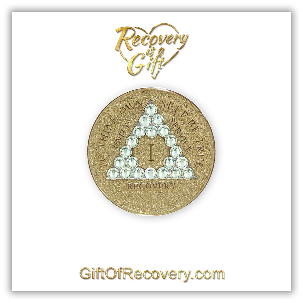 1 year AA medallion in gold glitter with twenty-one genuine clear CZ crystals in the shape of a triangle, symbolizing transformation under pressure, to thine own self be true, unity, service, recovery and roman numeral are embossed with 14k gold-plated brass along with outer rim, sealed in a chip and scratch-resistant resin giving it a beautiful glossy look, recovery medallion is featured on a white 3x3 card with recovery is a gift going through a heart at the top and giftofrecovery.com at the bottom.