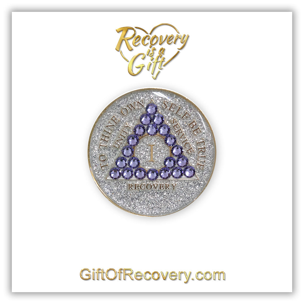 1 year AA medallion silver glitter with 21 purple genuine crystals in the shape of a triangle, to thine own self be true, unity, service, recovery, and roman numeral are embossed with 14k gold-plated brass, sealed in a high-quality, chip and scratch-resistant resin dome giving it a beautiful glossy look that will last, recovery medallion is featured on a white 3x3 card with recovery is a gift going through a heart at the top center and giftofrecovery.com bottom center, both in the color gold.