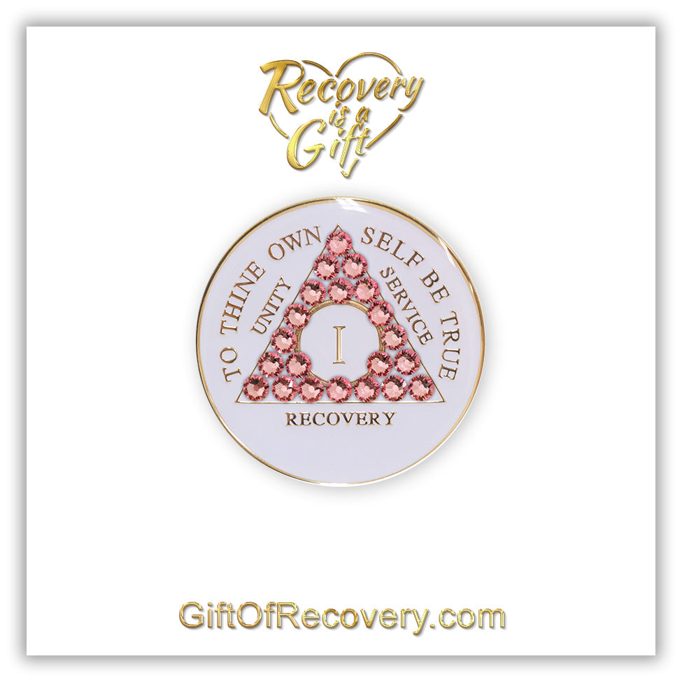 1 year pearl white AA medallion with Twenty-one genuine rose crystals in the shape of the triangle, unity, service, recovery, roman numeral, and to thine own self be true, embossed in 14k gold-plated brass and sealed with resin for a glossy finish that is scratch proof and will last, the recovery medallion is featured on a white 3x3 card with recovery is a gift in a heart at the top and giftofrecovery.com at the bottom, both are in the color gold.