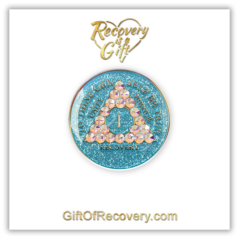 1 year deep sea aqua glitter AA medallion adorned with 21 genuine Aurora Borealis crystals representing the different colors and stages of our new lives, to thine own self be true, unity, service, recovery are embossed with 14k gold-plated brass and sealed with resin for a glossy finish that is scratch proof and will last, seen on a white 3x3 card with recovery is a gift going through an open heart at the top and giftofrecovery.com on the bottom, both in the color gold. 