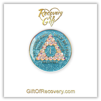 1 year deep sea aqua glitter AA medallion adorned with 21 genuine Aurora Borealis crystals representing the different colors and stages of our new lives, to thine own self be true, unity, service, recovery are embossed with 14k gold-plated brass and sealed with resin for a glossy finish that is scratch proof and will last, seen on a white 3x3 card with recovery is a gift going through an open heart at the top and giftofrecovery.com on the bottom, both in the color gold. 