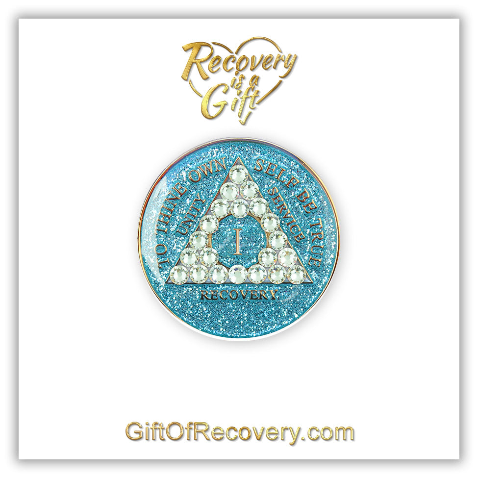 1 year deep sea Aqua glitter AA medallion adorned with 21 diamond CZ genuine crystals in the shape of the triangle, to thine own self be true, unity, service, recovery are embossed with 14k gold-plated brass and sealed with resin for a lasting finish, featured on a white 3x3 card, recovery is a gift at the top going through an open heart and giftofrecovery.com at the bottom, both in the color gold. 