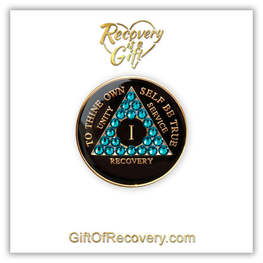 1 Year Recovery Medallion Black Onyx with twenty-one Blue zircon crystals in the shape of the triangle, with to thine own self be true, roman numeral, and unity, service, recovery embossed with 14k Gold-plated brass, the medallion is featured on a white 3x3 card with recovery is a gift and giftofrecovery.com in the color gold. 