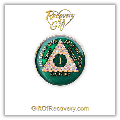 1 year AA medallion Emerald green with 21 genuine Aurora Borealis CZ crystals that make the triangle, to symbolize new beginnings and to dance in the sunlight once again, AA slogan and three legacies are embossed with 14k gold-plated brass and sealed for a glossy finish that will last, pictured on a white 3x3 card with recovery is a gift going through an open heart at the top and giftofrecovery.com at the bottom, both in the color gold.