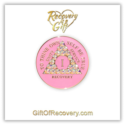 1 Year AA medallion princess pink with 21 Aurora Borealis CZ genuine crystals symbolizing beauty and change from working the program, AA slogan and 3 legacies are embossed with 14k gold-plated brass, sealed with resin for a lasting finish, seen on a white 3x3 card with recovery is a gift going through an open heart at the top and giftofrecovery.com at the bottom, both in the color gold. 