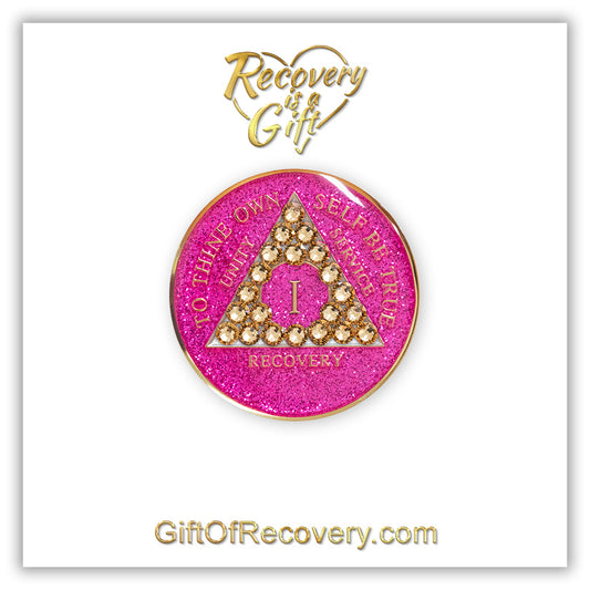 1 year AA recovery medallion in glitter princess pink and adorned with 21 gold CZ genuine crystals shaped in the triangle to add sparkle to your sober princess journey in recovery, to thine own self be true, unity, service, recovery are embossed with 14k gold-plated brass and sealed with resin for a glossy finish that will last and is scratch proof, featured on a white 3x3 card with recovery is a gift, giftofrecovery.com in the color gold.