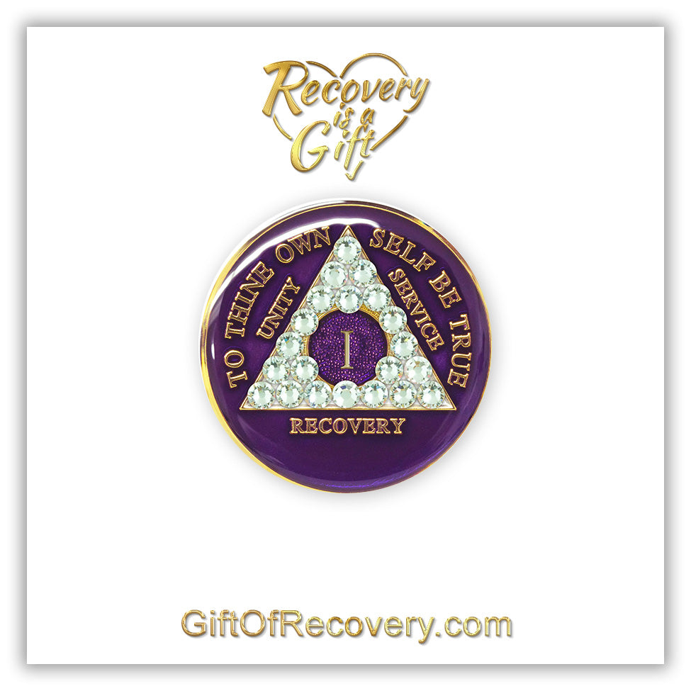 1 year AA medallion purple amethyst, adorned with 21 genuine diamond CZ crystals to represent transformation under pressure in the recovery journey, to thine own self be true, unity, service, recovery embossed with 14k gold-plated brass and sealed with resin for a glossy finish that is scratch proof and will last, the recovery medallion is featured on a white 3x3 card, recovery is a gift going through an open heart at the top and giftofrecovery.com on the bottom, in the color gold.