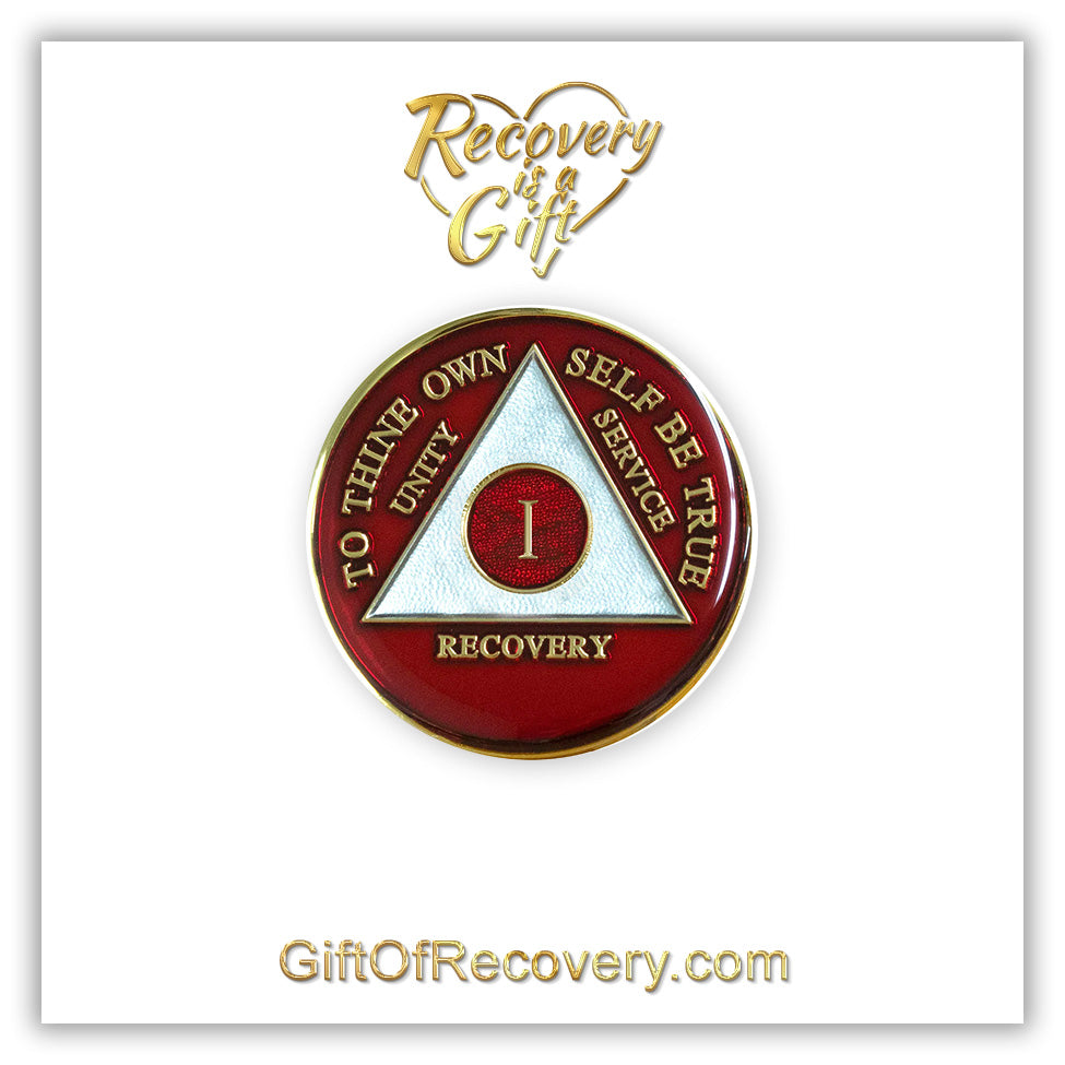 1 year AA medallion Ruby red, ignite the fire in your recovery and keep it lit, triangle is pearl white, to thine own self be true, unity, service, recovery, and roman numeral are embossed with 14k gold-plated brass, the recovery medallion is sealed with resin for a glossy finish that will last and is scratch free, pictured on a white 3x3 card with recovery is a gift going through an open heart at the top and giftofrecovery.com on the bottom, both in the color gold.