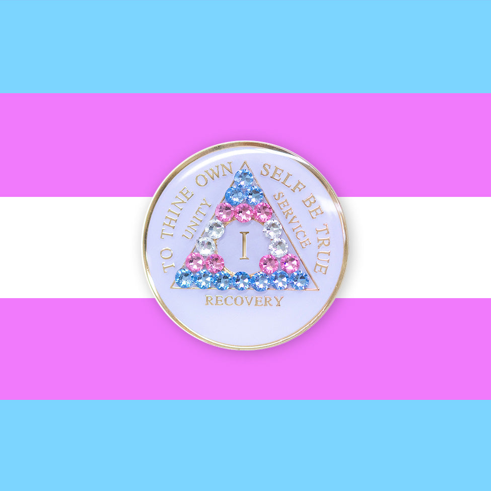 1 Year AA medallion pearl white with 21 genuine crystals that are the colors of the Transgender flag, to represent sobriety and pride for who you are, AA slogan and three legacies are embossed with 14k gold-plated brass and recovery medallion is sealed with resin for a glossy finish, pictured on a 3x3 example of the Transgender flag.