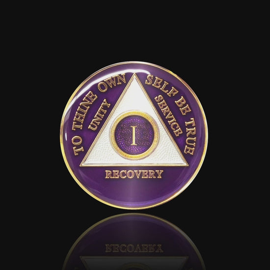 1 year AA medallion Amethyst purple, recovery is possible, triangle is pearl white, to thine own self be true, unity, service, recovery, and roman numeral are embossed with 14k gold-plated brass, the recovery medallion is sealed with resin for a glossy finish that will last and is scratch free, featured in a 15 second video with a black background.