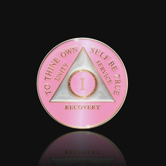 1 year AA medallion Princess pink, the ultimate girl medallion, show off your feminine side, triangle is pearl white, to thine own self be true, unity, service, recovery, and roman numeral are embossed with 14k gold-plated brass, the recovery medallion is sealed with resin for a glossy finish that will last and is scratch free, featured in a 15 second video with a black background.