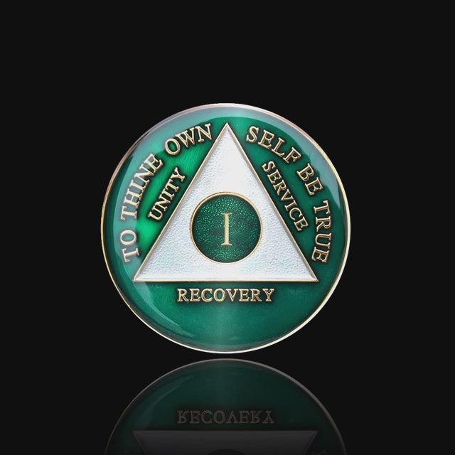 1 year AA medallion Emerald green, triangle is pearl white, to thine own self be true, unity, service, recovery, and roman numeral are embossed with 14k gold-plated brass, the recovery medallion is sealed with resin for a glossy finish that will last and is scratch free, featured in a 15 second video with a black background.