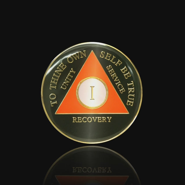 1 year AA medallion black Onyx, triangle is orange, to thine own self be true, unity, service, recovery, and roman numeral are embossed with 14k gold-plated brass, the recovery medallion is sealed with resin for a glossy finish that will last and is scratch free, featured in a 15 second video with a black background.