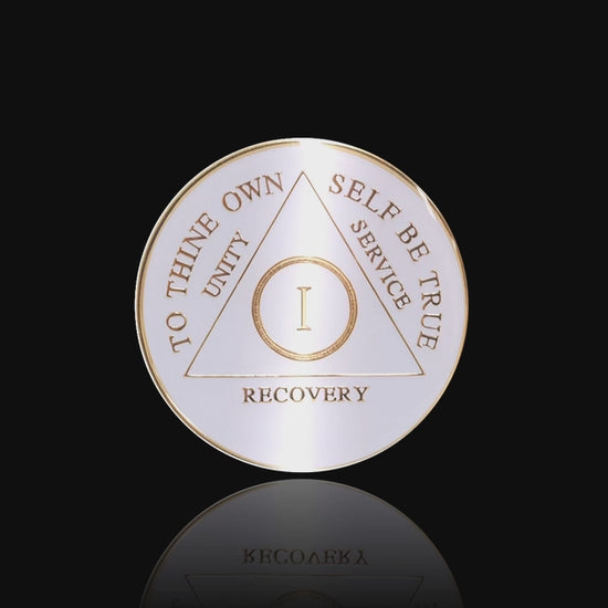 1 year AA medallion pearl white, to symbolize getting a new clean slate in recovery, to thine own self be true, unity, service, recovery, and roman numeral are embossed with 14k gold-plated brass, the recovery medallion is sealed with resin for a glossy finish that will last and is scratch free, featured in a 15 second video with a black background.