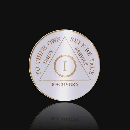 1 year AA medallion pearl white, to symbolize getting a new clean slate in recovery, to thine own self be true, unity, service, recovery, and roman numeral are embossed with 14k gold-plated brass, the recovery medallion is sealed with resin for a glossy finish that will last and is scratch free, featured in a 15 second video with a black background.