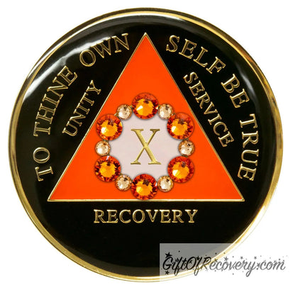 Recovery medallion 10 year black onyx 12 crystals that form the circle around the roman numeral representing growth in recovery, the triangle is sunset orange and the circle is pearl white, the lettering is embossed with 14k gold-plated brass and sealed in resin for a glossy finish that is scratch resistant.