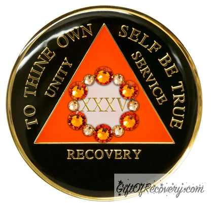 Recovery medallion 35 year black onyx 12 crystals that form the circle around the roman numeral representing growth in recovery, the triangle is sunset orange and the circle is pearl white, the lettering is embossed with 14k gold-plated brass and sealed in resin for a glossy finish that is scratch resistant.