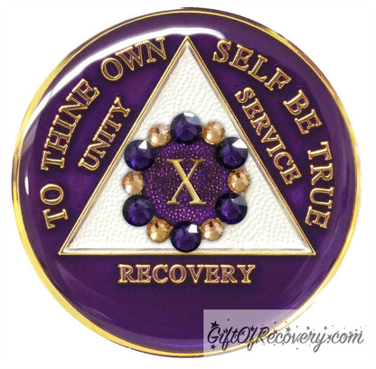 10 year AA medallion purple Amethyst adorned with 6 gold and 6 purple genuine crystal in a circle around the roman numeral to symbolize a flower and to bloom where planted in your recovery journey, triangle is pearl white and AA moto is embossed with 14k gold-plated brass, sealed in resin for a glossy finish that will last and is scratch proof.