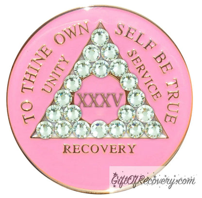 35 year AA medallion princess pink the triangle is adorned with 21 diamond CZ genuine crystals that represent transformation under pressure, the AA slogan and three legacies are embossed with 14k gold-plated brass, the recovery medallion is sealed with resin for a lasting finish.