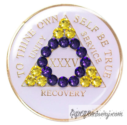 35 year AA medallion pearl white with 21 genuine crystals that form the triangle and are in the color of the intersex flag, colors are yellow and purple, to represent pride and sobriety, the AA slogan and three legacies are embossed with 14k gold-plated brass and sealed with resin for a glossy finish that will last and is scratch proof.