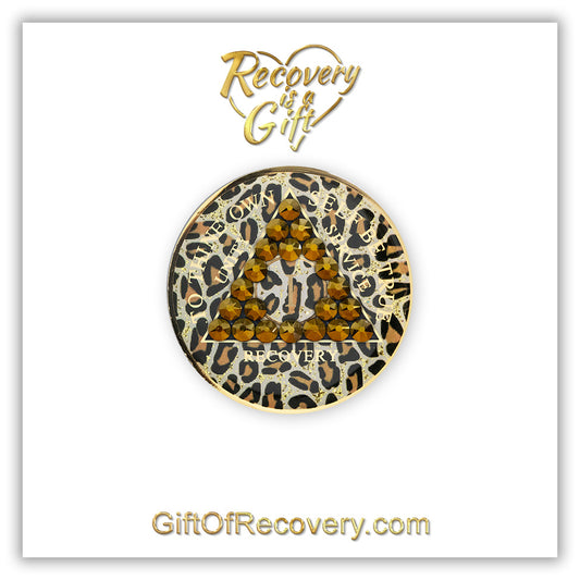 1 year AA medallion in leopard print with gold flake glitter spots and 21 genuine dorado crystals shaped in a triangle around the year, the outer rim is 14k gold and the unity, service, recovery, To thine own self be true and the year is 14k gold foil, the recovery medallion is set on a white 3x3 card and has recovery is a gift going through a heart shape and giftofrecovery.com in color gold. 