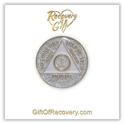 1 year AA medallion Glitter silver, always shine on in sobriety, triangle is pearl white, to thine own self be true, unity, service, recovery, and roman numeral are embossed with 14k gold-plated brass, the recovery medallion is sealed with resin for a glossy finish that will last and is scratch free, pictured on a white 3x3 card with recovery is a gift going through an open heart at the top and giftofrecovery.com on the bottom, both in the color gold.